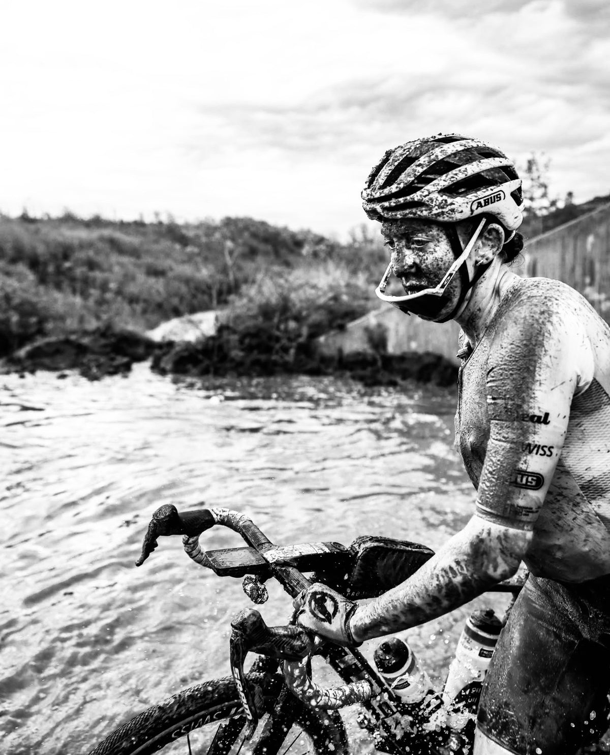 Ciclista cubierta de barro junto a un cruce de agua en Unbound Gravel 2026