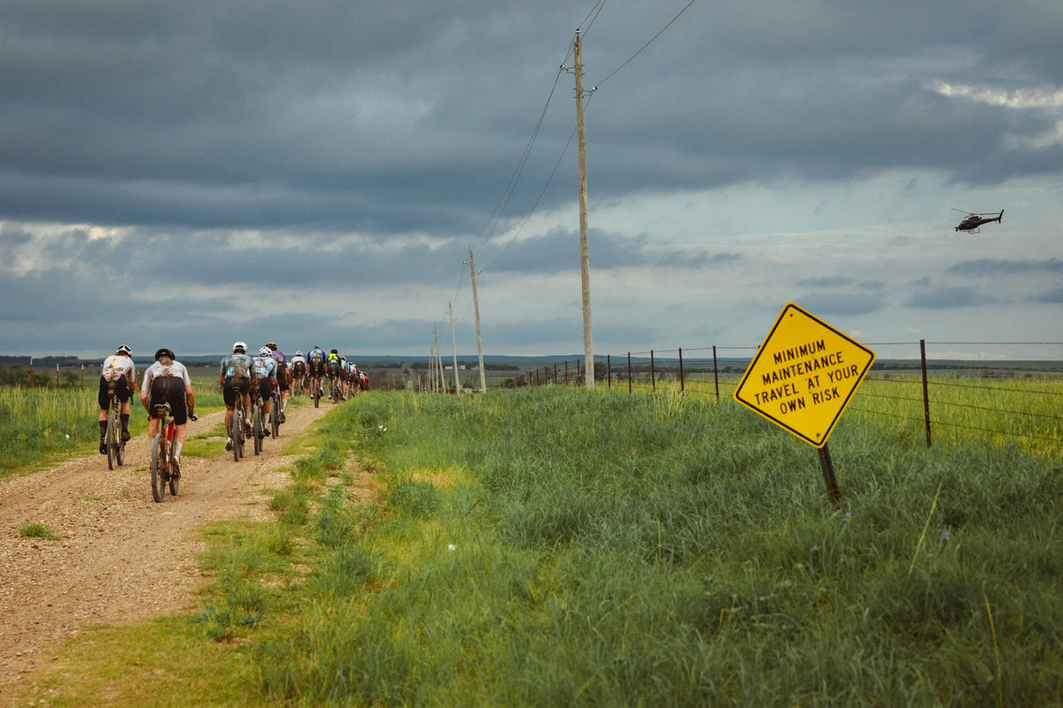 Ciclistas de Unbound Gravel junto a una señal de Minimum Maintenance en Kansas